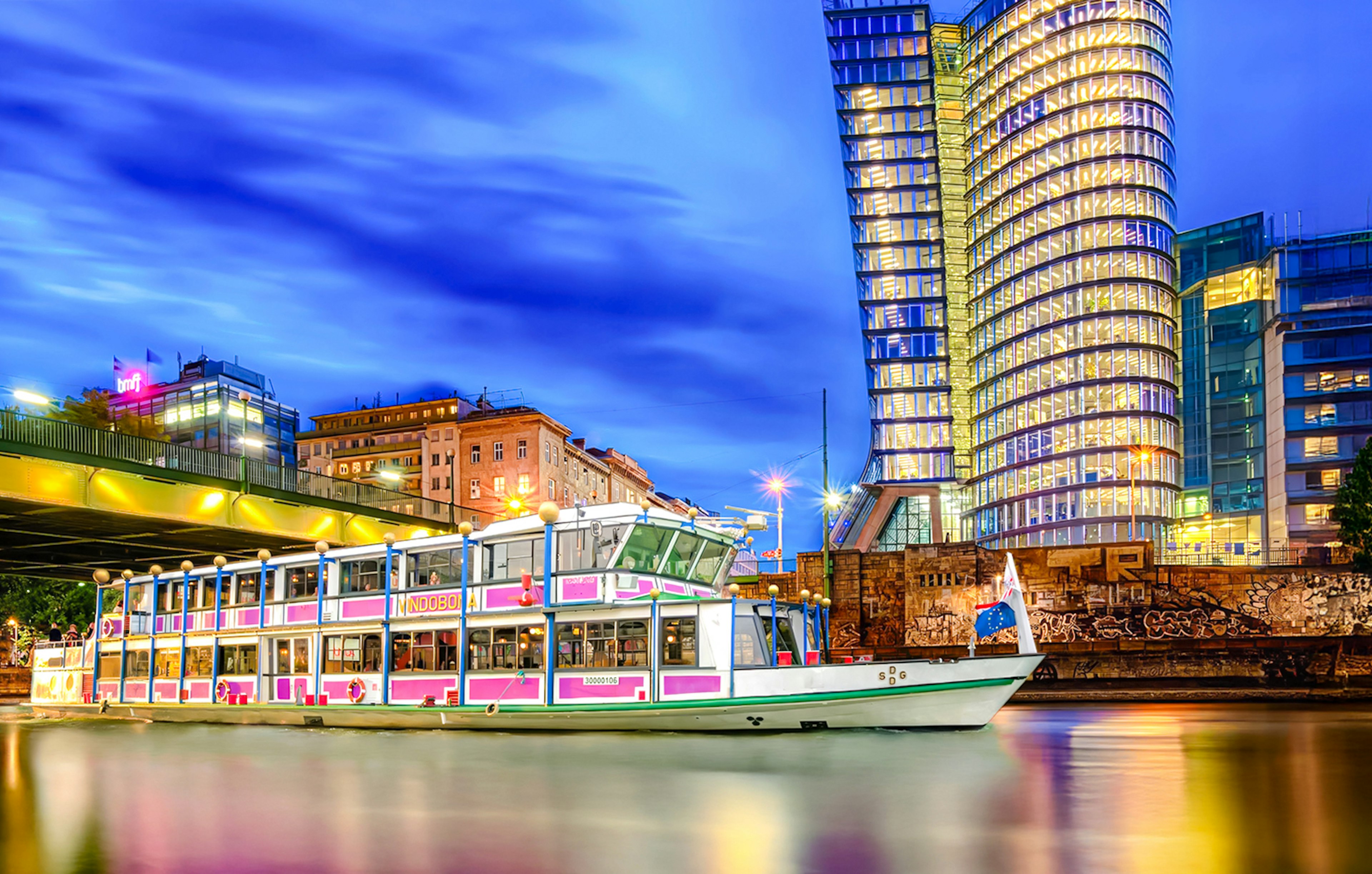 Evening cruise boat on Danube River with illuminated cityscape in the background.