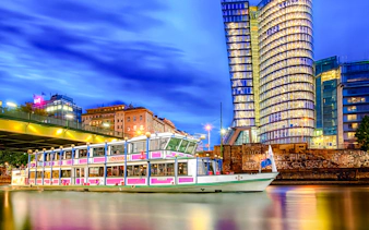 Evening cruise boat on Danube River with illuminated cityscape in the background.