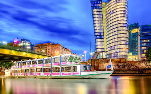 Evening cruise boat on Danube River with illuminated cityscape in the background.