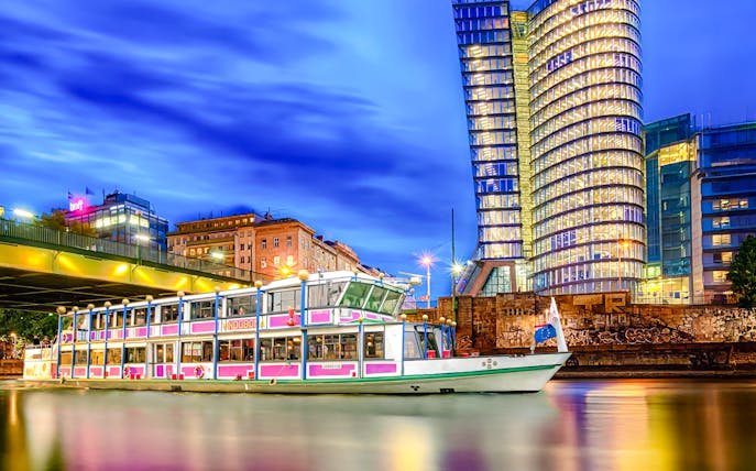 Evening cruise boat on Danube River with illuminated cityscape in the background.