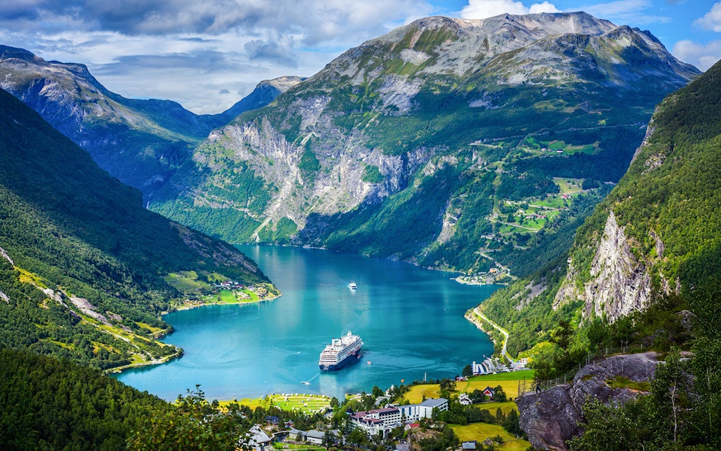 Cruise ship sailing through Geiranger Fjord, surrounded by mountains and lush greenery in Norway.