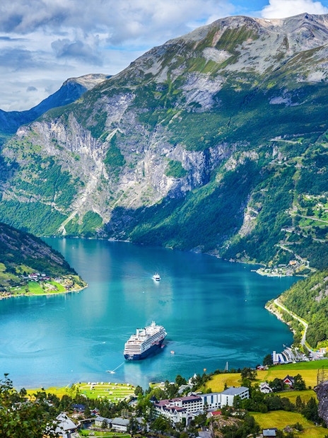 Cruise ship sailing through Geiranger Fjord, surrounded by mountains and lush greenery in Norway.