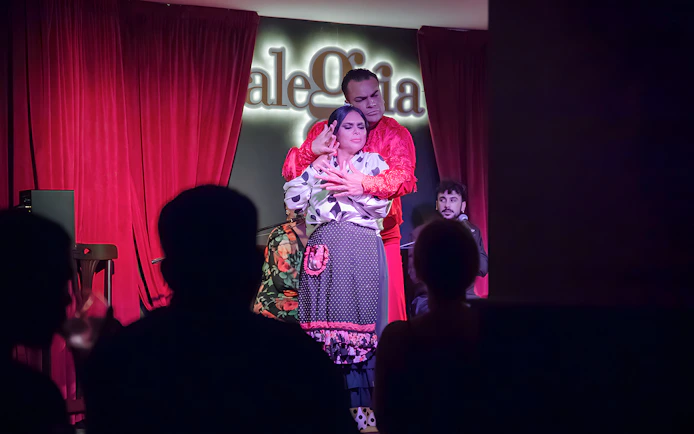 Flamenco dancers performing at Alegría with red curtains in the background.