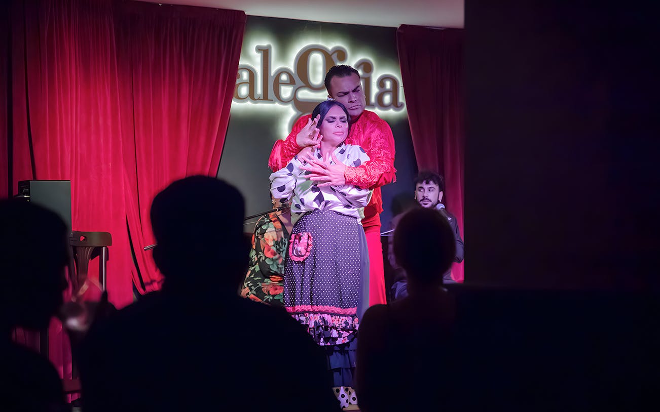 Flamenco dancers performing at Alegría with red curtains in the background.
