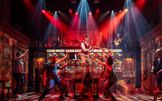 Performers on stage during The Choir of Man show, with vibrant lighting and musical instruments.