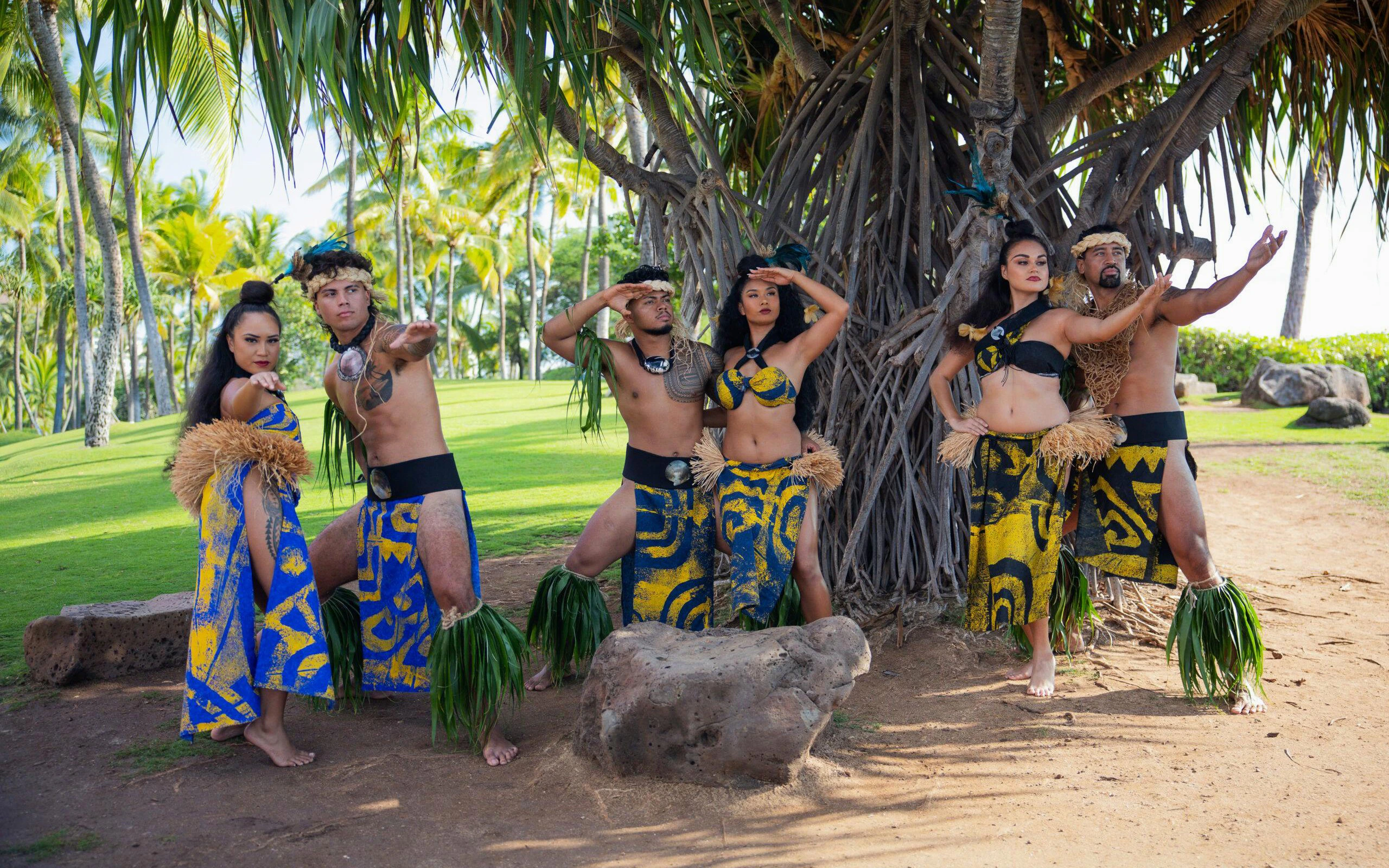 Performers in traditional attire at a Kaula-Luau, Hawaii, under palm trees.