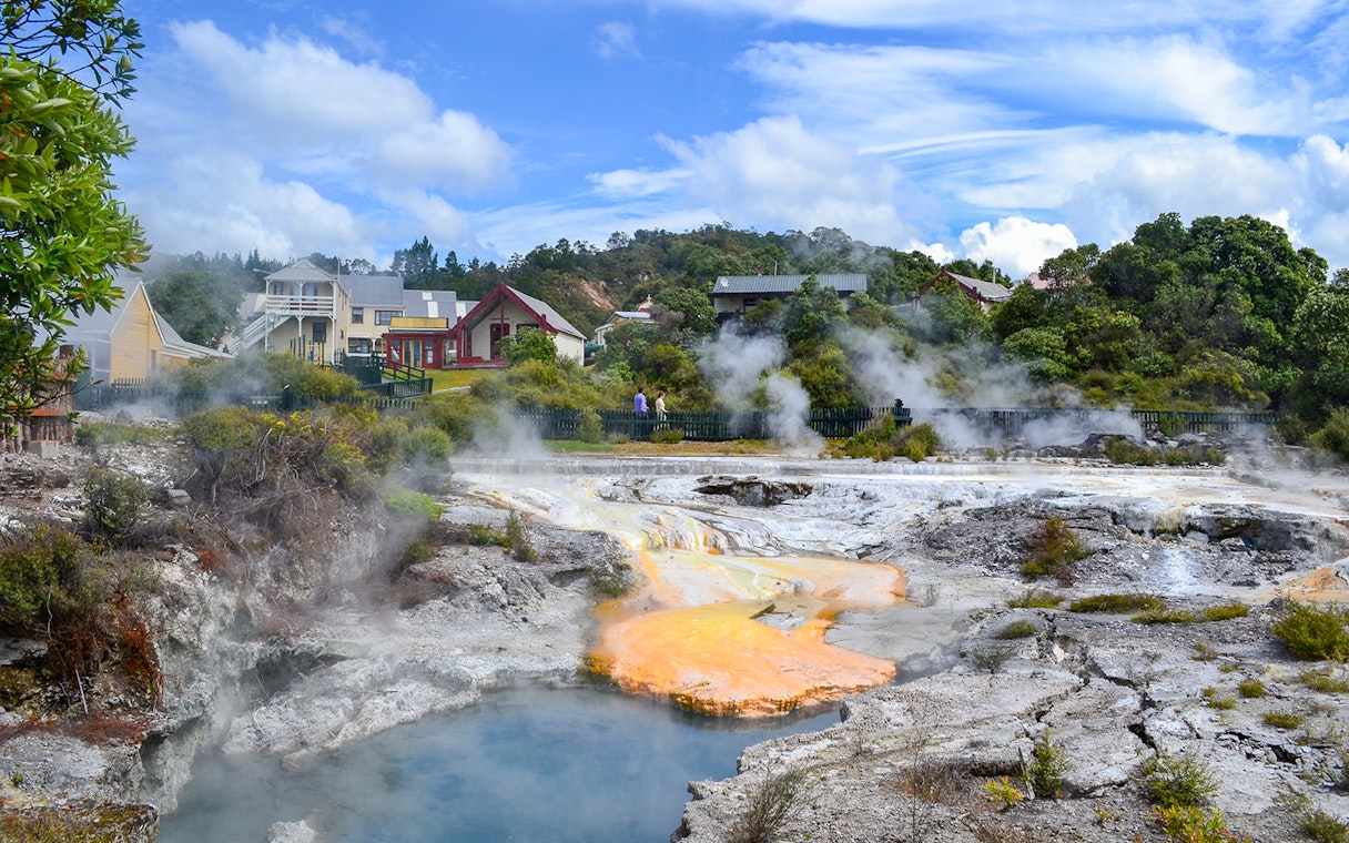 Whakarewarewa geothermal area with steam rising near Maori village buildings.