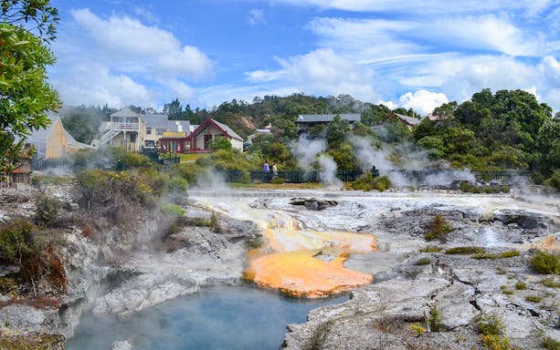 Whakarewarewa geothermal area with steam rising near Maori village buildings.