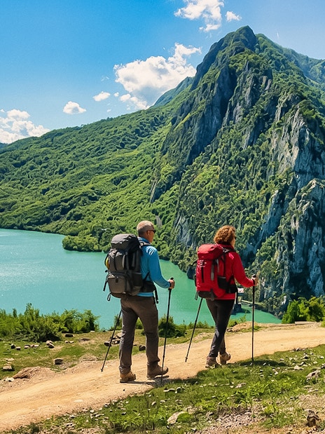 Guests hiking near Bovilla Lake with Gamti Mountains in the background.