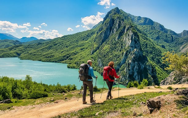 Guests hiking near Bovilla Lake with Gamti Mountains in the background.