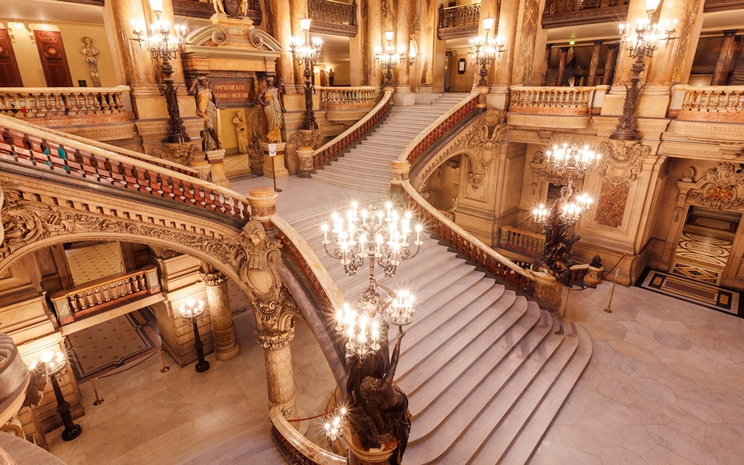 Opera Garnier's grand staircase with ornate chandeliers and intricate architectural details.