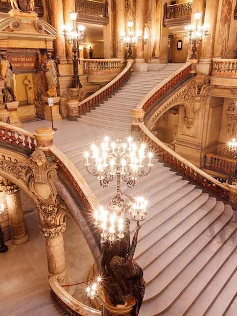 Opera Garnier's grand staircase with ornate chandeliers and intricate architectural details.