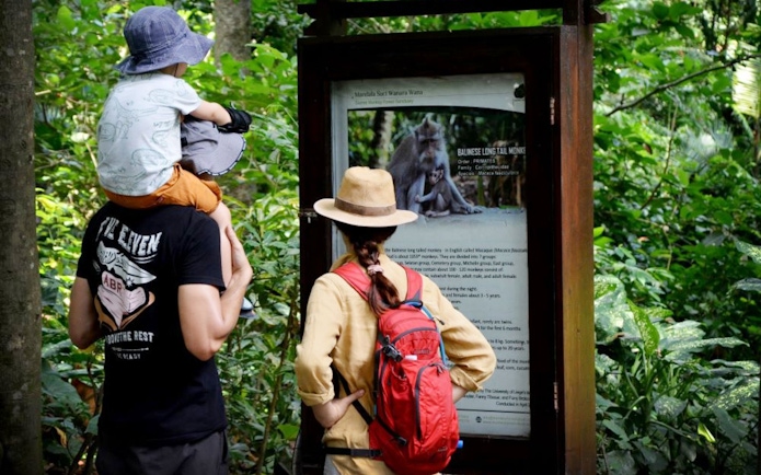 Visitors reading information board at Sacred Monkey Forest Ubud, surrounded by lush greenery.