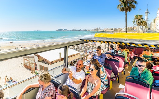 Open-top bus tour along Cadiz beach with passengers enjoying the view.