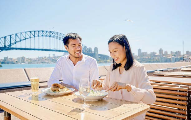 Couple dining outdoors with Sydney Harbour Bridge in the background.