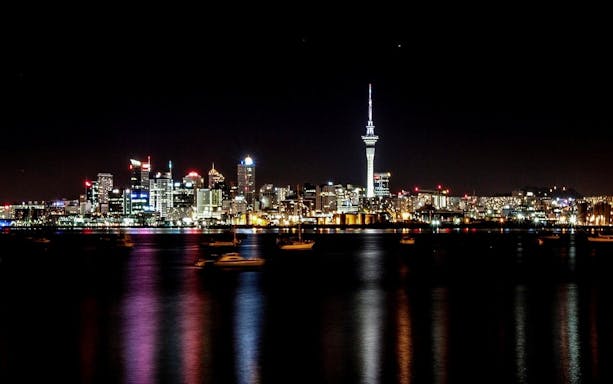 Auckland skyline at night with illuminated Sky Tower and reflections on the harbor.