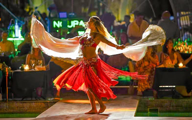Performer dancing at Nouba Restaurant Dinner Show with vibrant red costume.