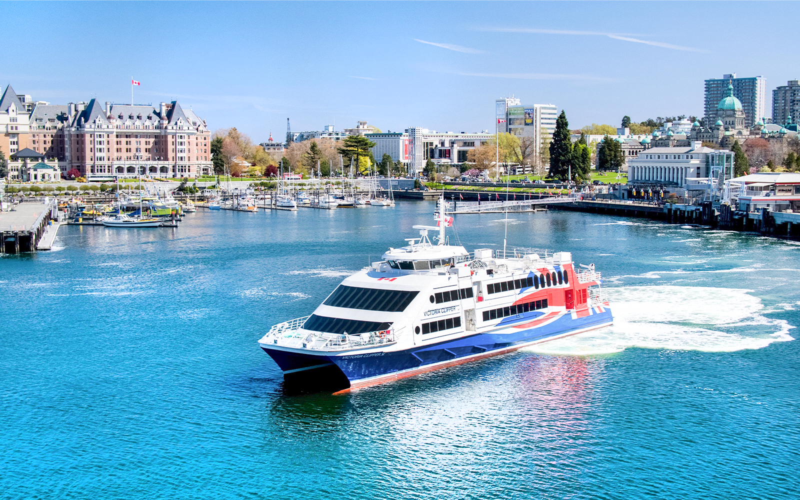High-speed ferry in Victoria harbor with cityscape and marina views.