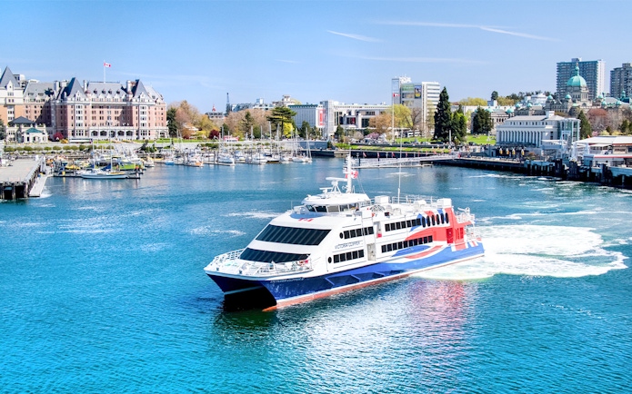 High-speed ferry in Victoria harbor with cityscape and marina views.