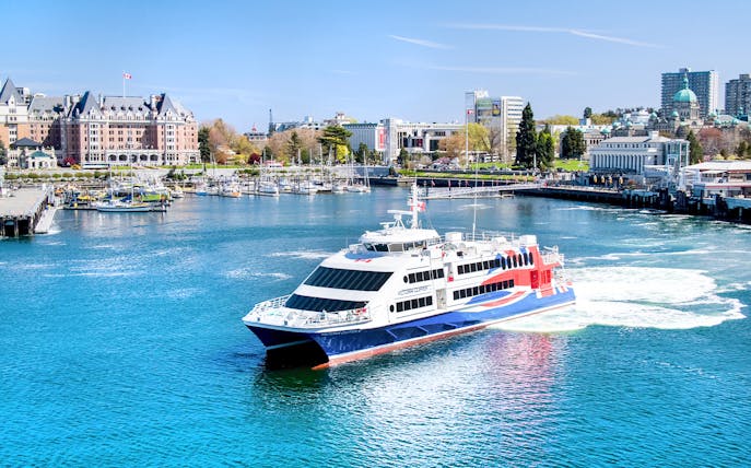 High-speed ferry in Victoria harbor with cityscape and marina views.