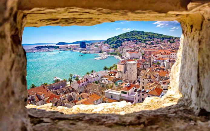 View of Split, Croatia from a stone window, featuring the coastline and historic buildings.