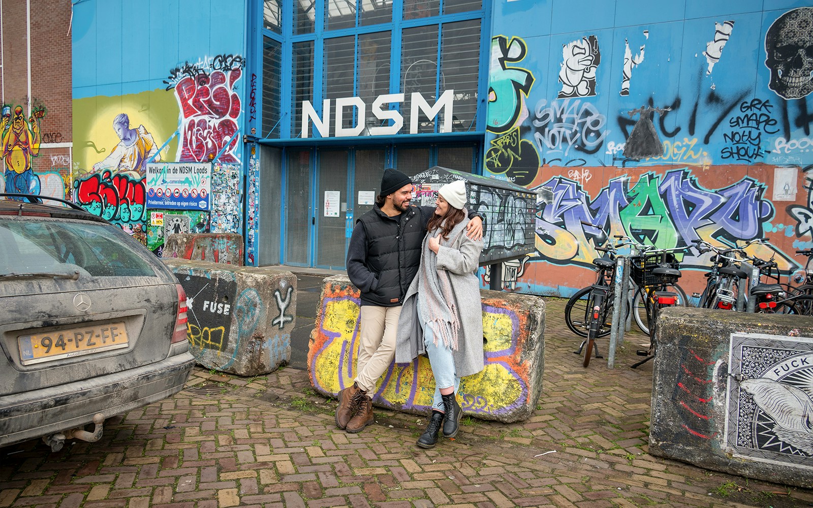Couple posing in front of graffiti at NDSM, Amsterdam during a professional photoshoot.