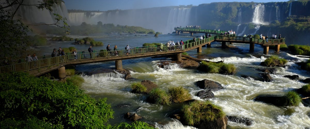 Walkway over Iguazu Falls with tourists viewing waterfalls, Brazil-Argentina border.