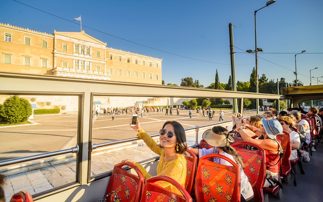 HOHO tour bus passing by the Greek Parliament in Athens, with tourists taking photos.