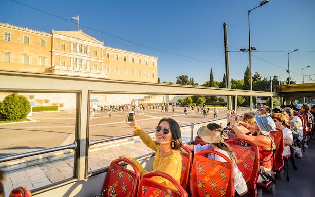 HOHO tour bus passing by the Greek Parliament in Athens, with tourists taking photos.