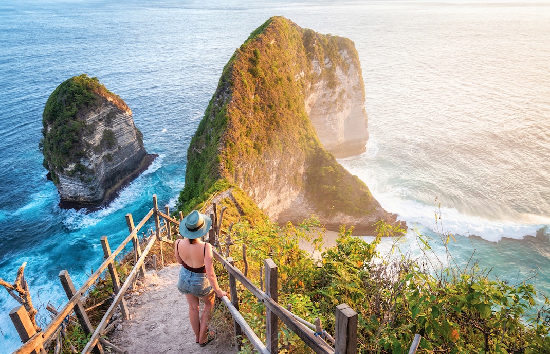 Woman walking down stairs towards Kelingking Beach cliffs on Nusa Penida Island, Indonesia.