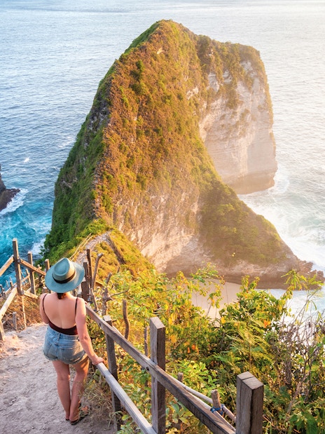 Woman walking down stairs towards Kelingking Beach cliffs on Nusa Penida Island, Indonesia.