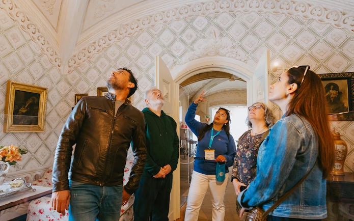 Tour group inside Pena Palace, Sintra, observing ornate ceiling details.
