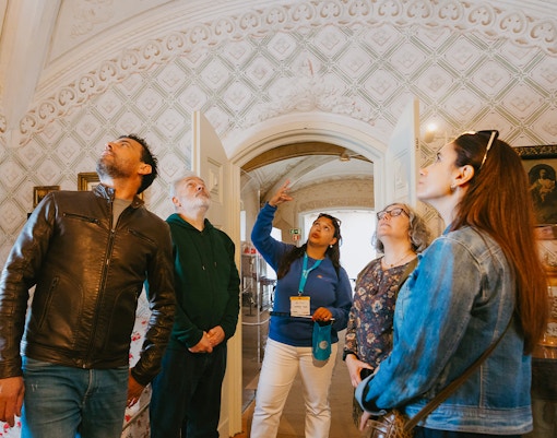Tour group inside Pena Palace, Sintra, observing ornate ceiling details.