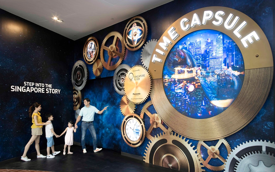 Family exploring Time Capsule exhibit at Singapore Flyer with cityscape display.
