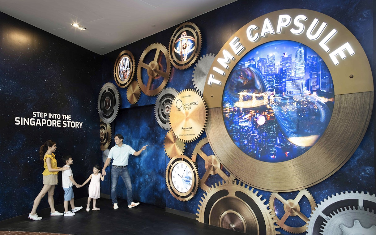 Family exploring Time Capsule exhibit at Singapore Flyer with cityscape display.