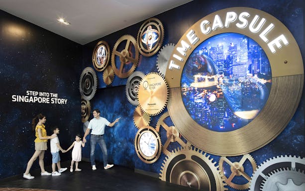 Family exploring Time Capsule exhibit at Singapore Flyer with cityscape display.