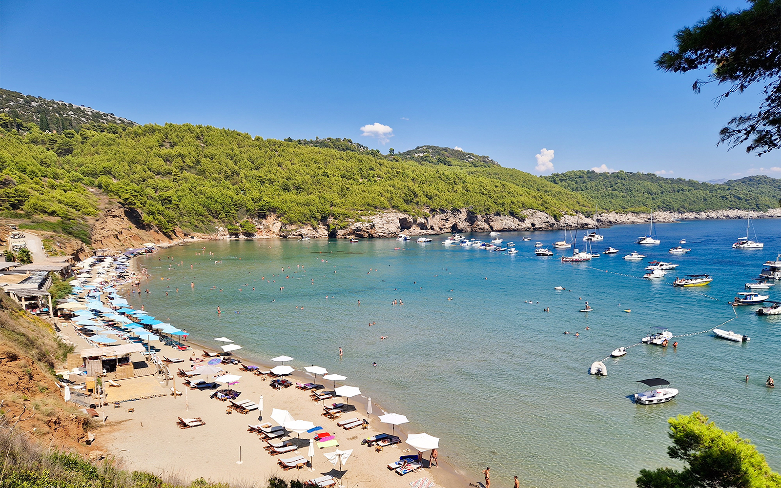 Sunj Beach on Lopud Island, Dubrovnik with sunbathers, umbrellas, and boats in the clear blue water.