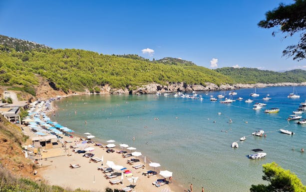 Sunj Beach on Lopud Island, Dubrovnik with sunbathers, umbrellas, and boats in the clear blue water.