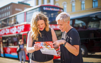 Guests checking hop on hop off bus schedule in front of a red double-decker bus.