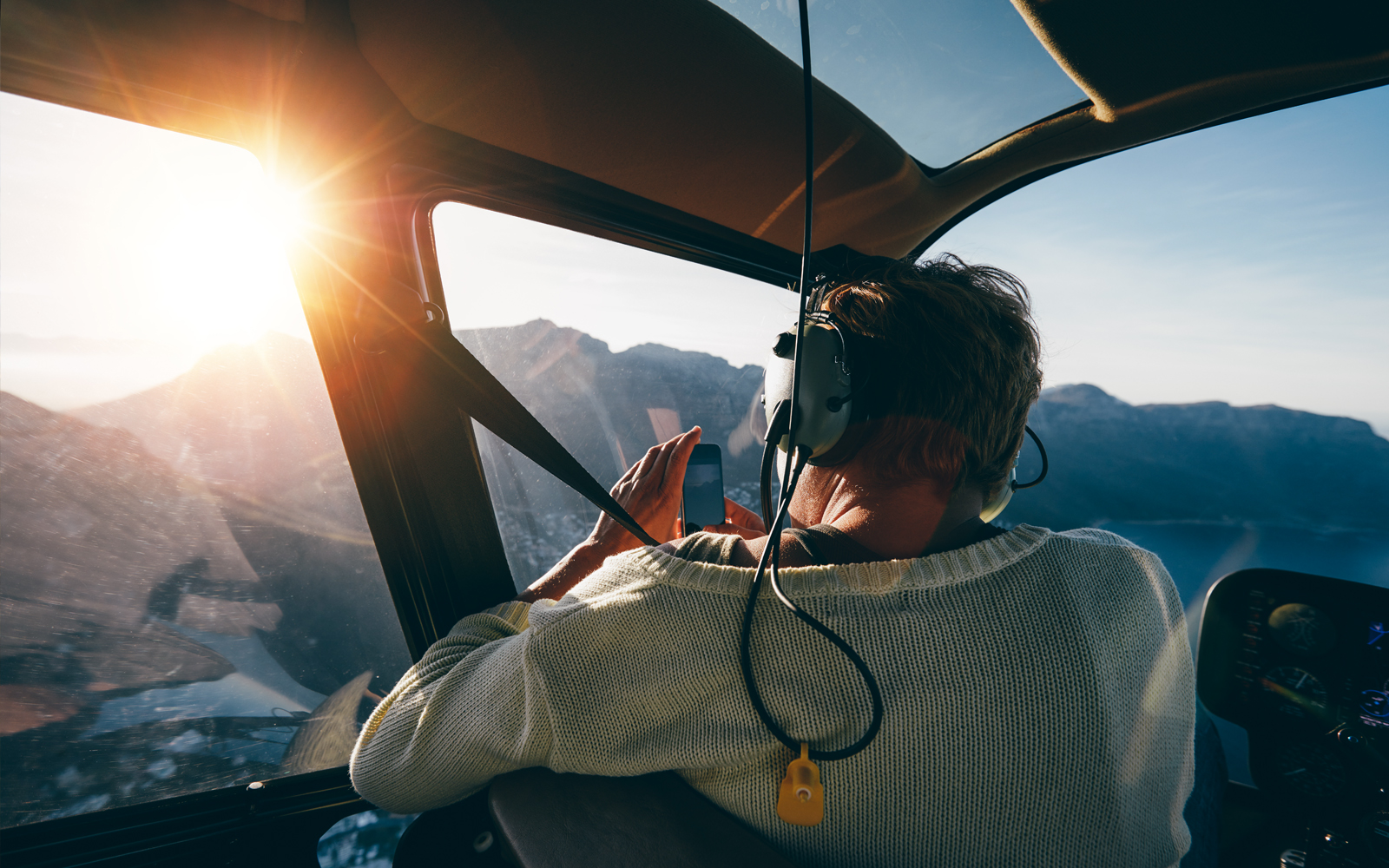 Helicopter passenger photographing mountain landscape at sunrise.