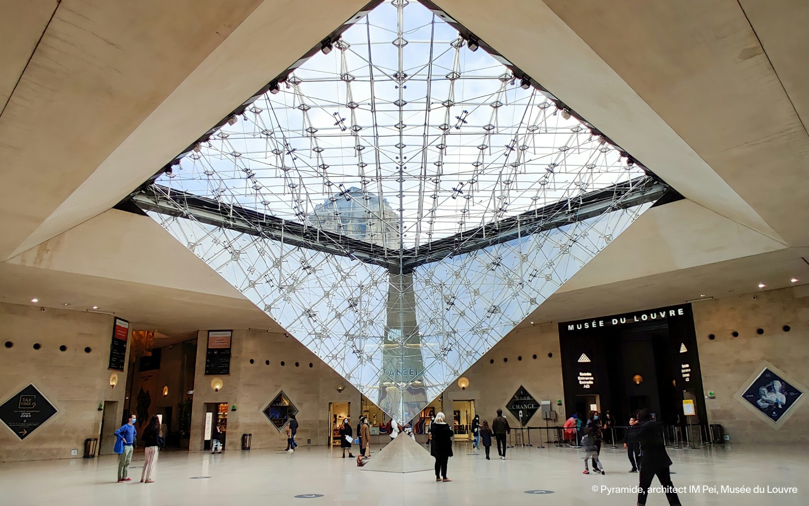 Louvre Museum entrance with Inverted Pyramid and visitors exploring the courtyard in Paris.