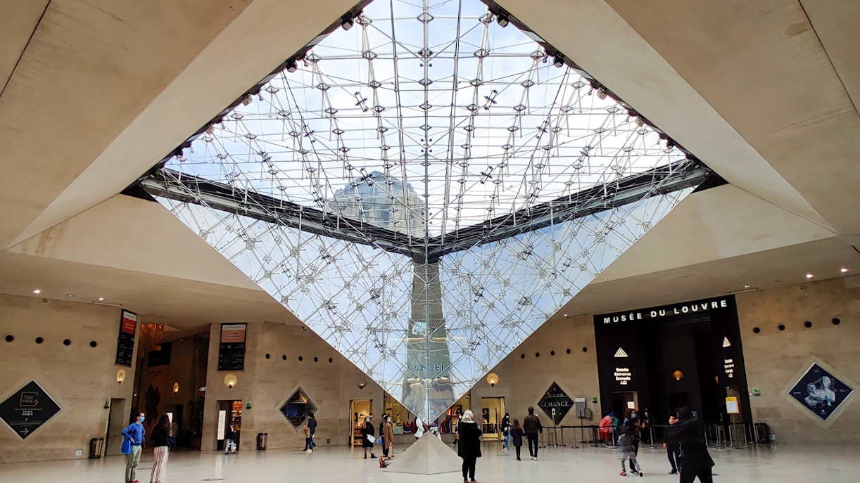 Louvre Museum entrance with Inverted Pyramid and visitors exploring the courtyard in Paris.