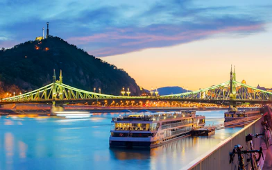 Liberty Bridge illuminated at dusk with Gellert Hill in the background, Budapest.