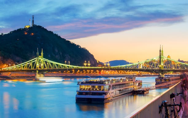 Liberty Bridge illuminated at dusk with Gellert Hill in the background, Budapest.