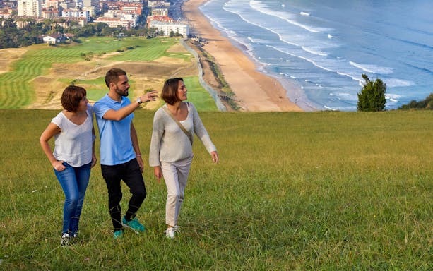 Tourists walking on a grassy hill overlooking Zarautz beach and town, Basque Country.