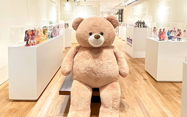 Giant teddy bear displayed at MINT Museum of Toys, Singapore, surrounded by vintage dolls.
