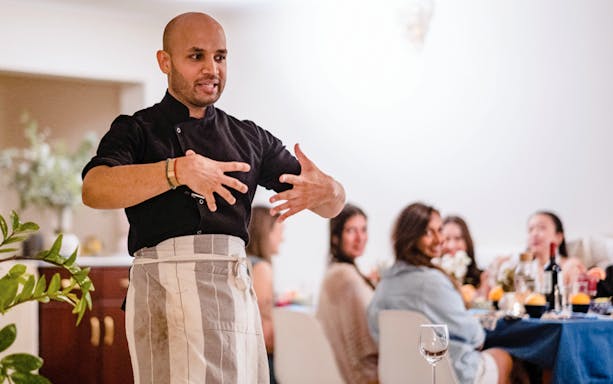 Chef presenting at Chef Kuv's Secret Supper with guests seated at a dining table.
