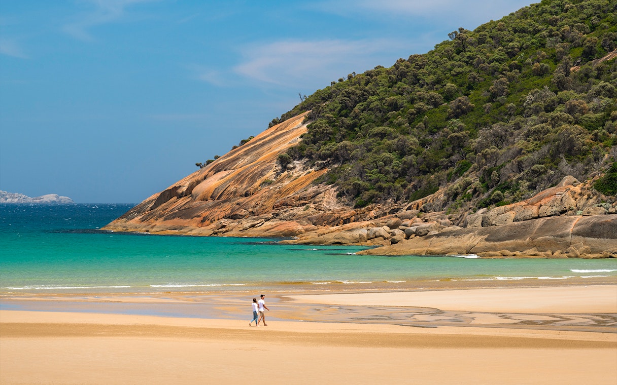 Couple walking on the beach at Wilsons Promontory National Park with scenic coastal view.