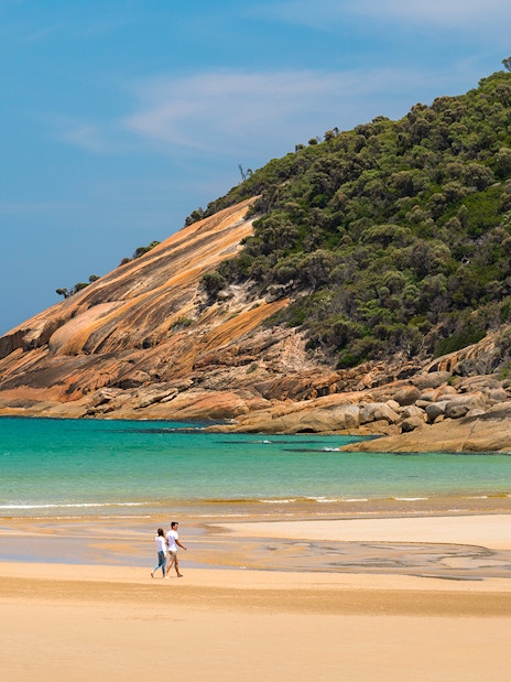 Couple walking on the beach at Wilsons Promontory National Park with scenic coastal view.