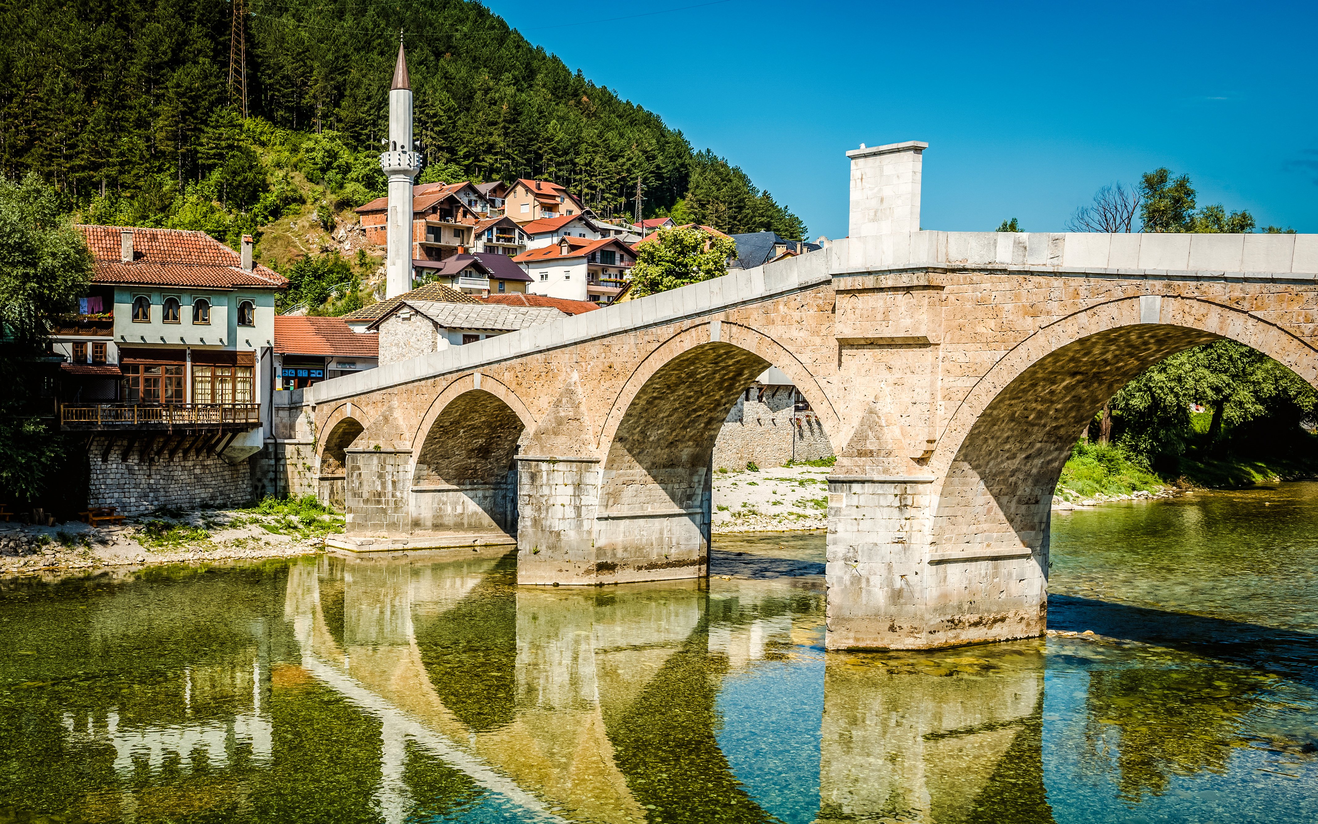 Old stone bridge over Neretva River in Konjic, Bosnia and Herzegovina with nearby houses.